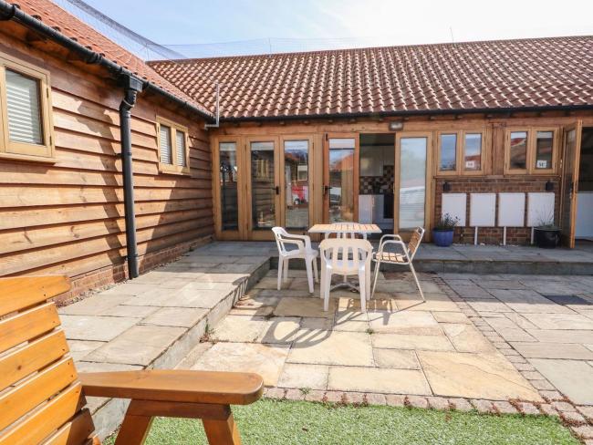 Exterior of a Hunstanton holiday cottage ovrlooking a paved courtyard with outdoor dining furniture