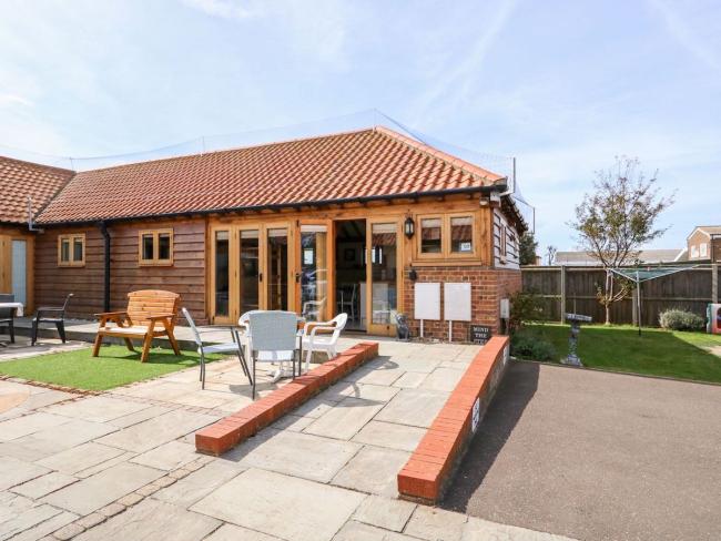 Exterior of a single-storey norfolk holiday cottage with outdoor seating and block-paved off-road parking.