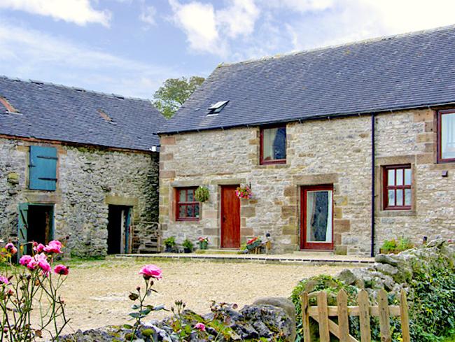 A stone-built cottage overlooks a cobbled courtyard bordered by a low stone wall.
