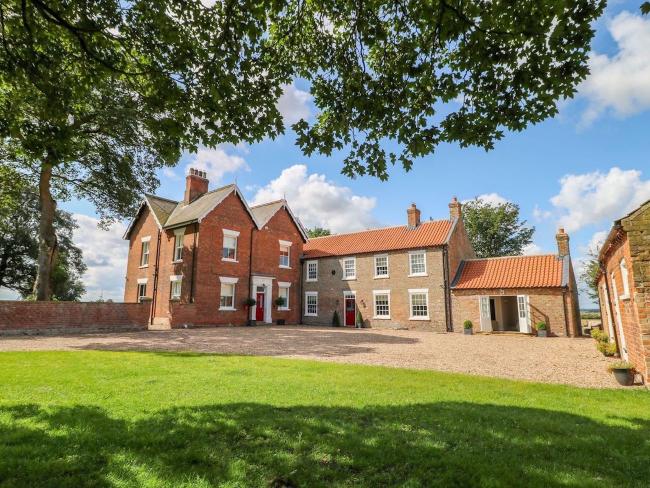 Exterior of a large, L-shaped brick East Yorkshire farmhouse overlooking a spacious courtyard and lawn.