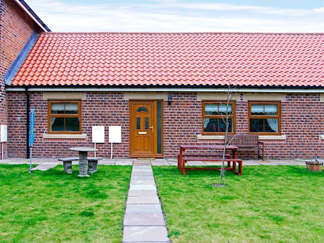 A paved footpath leads to the fron tdoor of a single-storey, brick-built Skinningrove holiday cottage