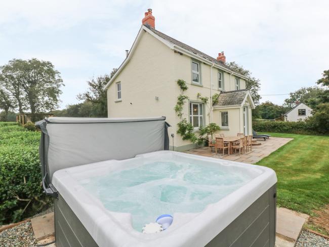 A hot tub bubbles away in in front of an elegant Pembrokeshire holiday cottage surrounded by  a patio and lawns.