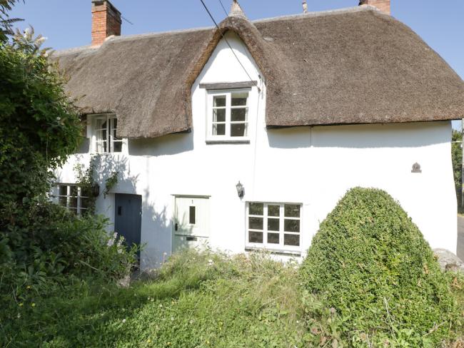 A thatched holiday cottage in Kilve overlooks a shrub-filled garden on the Somerset coast.