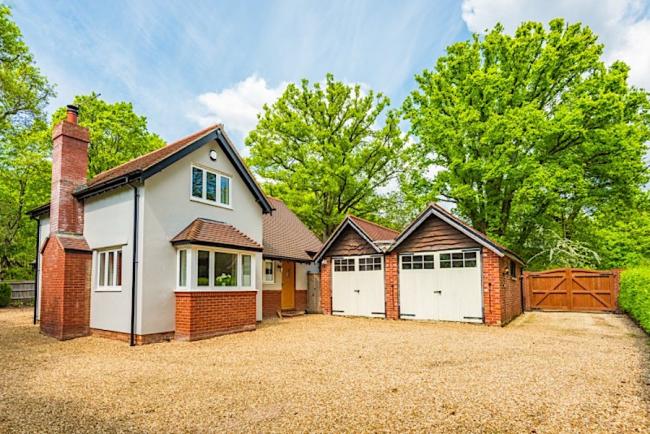 Exterior of a New Forest holiday cottage with a brick chimney stack, twin garages and backed by woodland trees.