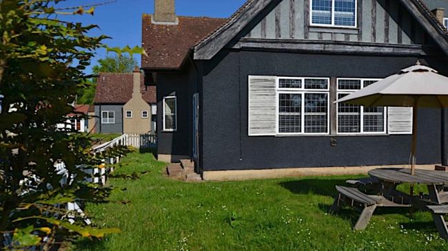 A two-storey Essex holiday cottage overlooking a lawn with a parasol on Osea Island