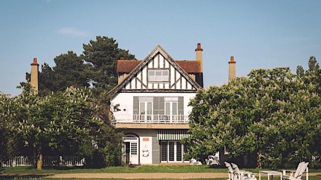 Gable end of a 3-storey period house with 2st floor balcony flanked by mature treees