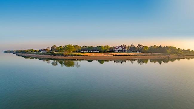 A flat tree-covered Islandreflected in a calm sea at sunset.