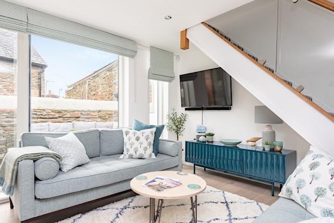 Carpeted lounge area with large windows in a Kingsbridge holiday cottage with sofa, large cupboard and coffee table