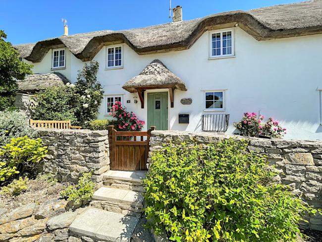 Exterior anf front garden of a double-fronted thatched holiday cottage in West Lulworth