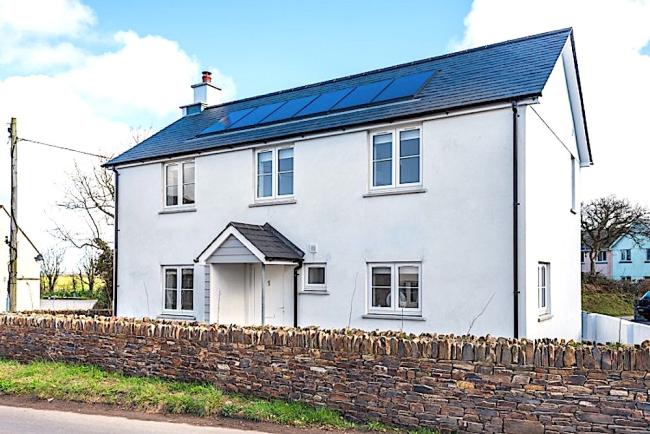 Exterior of a contemporary, slate-roofed holiday age surrounded by a low stone wall.