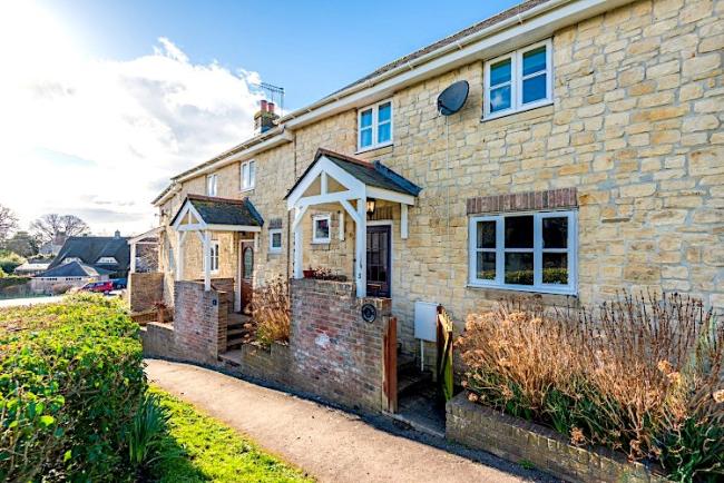 A limestone-built Dorset holiday cottage with a porch and tiny front garden.
