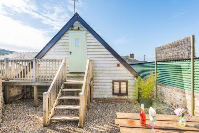 Gable end of a wood panelled Dorset barn conversion with wooden steps to a front door and deck.