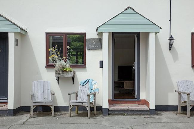 Wooden chair outside than open front door of a holiday cottage