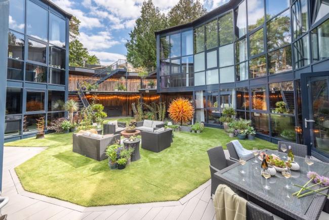 A 3-storey, glass-fronted house curves around a courtyard with a central lawn and sofas
