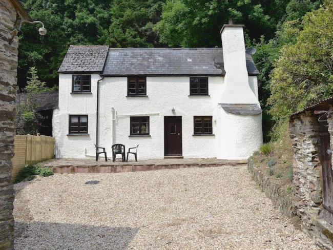 Exterior of an Exmoor country cottage with large chimney in front of tall trees and overlooking a large courtyard.