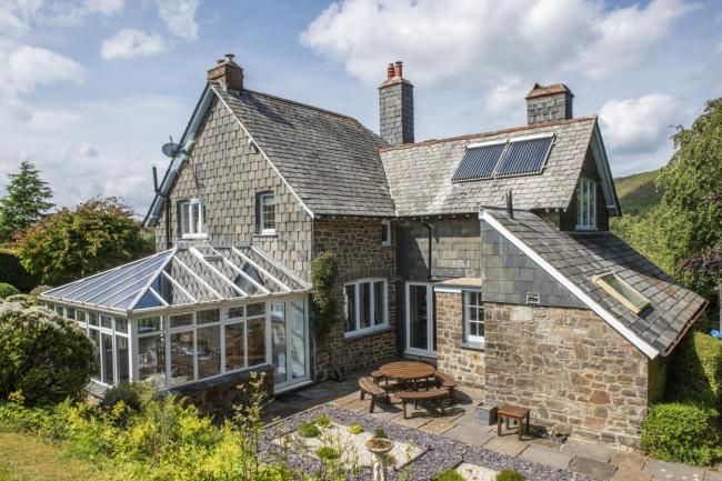 Exterior of a country house with sun room surrounded by beautiful gardens.