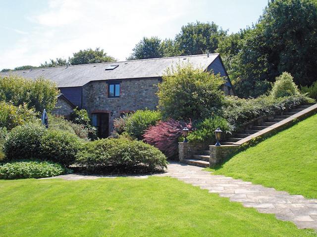 A stone-barn conversion surrounded by mature shrubs and trees.