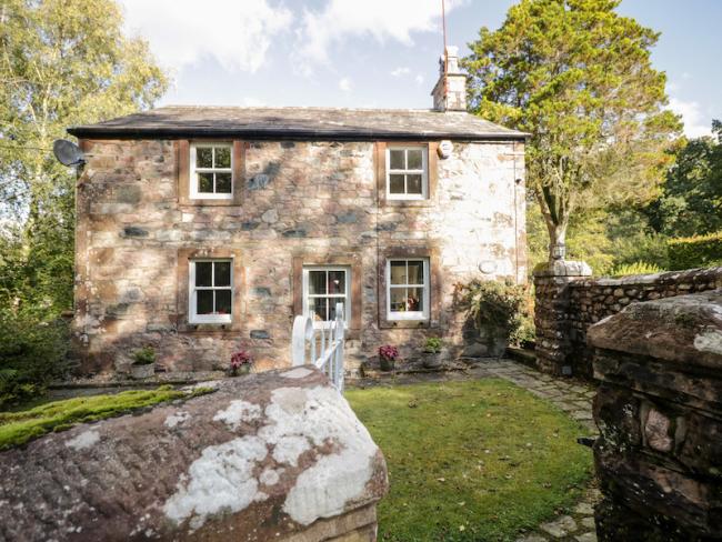 A stone-built, 2-storey cottage in Cumbria overlooks a large lawn.