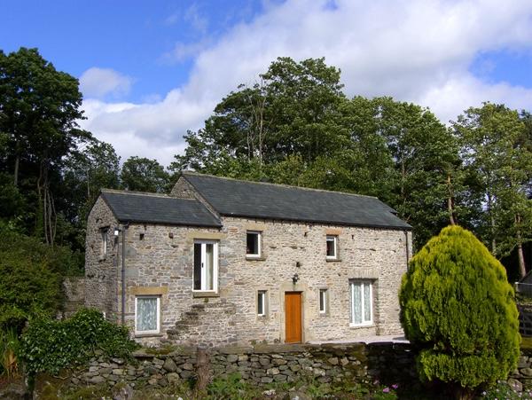 Doiuble-fronted exterior of a stone holiday cottage in Cumbria surrounded by mature trees.