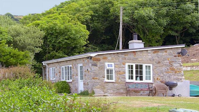 An Anglesey bungalow surrounded by lawns and a woodland backdrop.