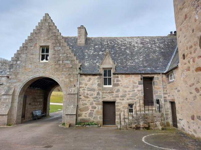 Entry arch and adjoining granite-built cottage overlook a castle courtyard. 