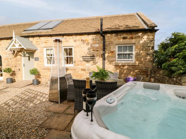 Exterior of a barn conversion overlooking a terrace with a hot tub.