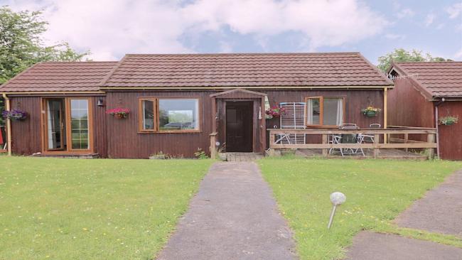 A single storey holiday bungalow with a patio and large lawn.