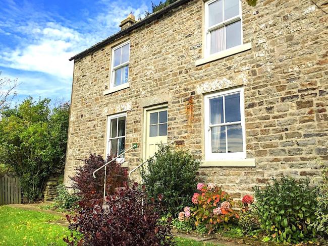 2-storey stone-built cottage overlooking a shrub-lined lawn.