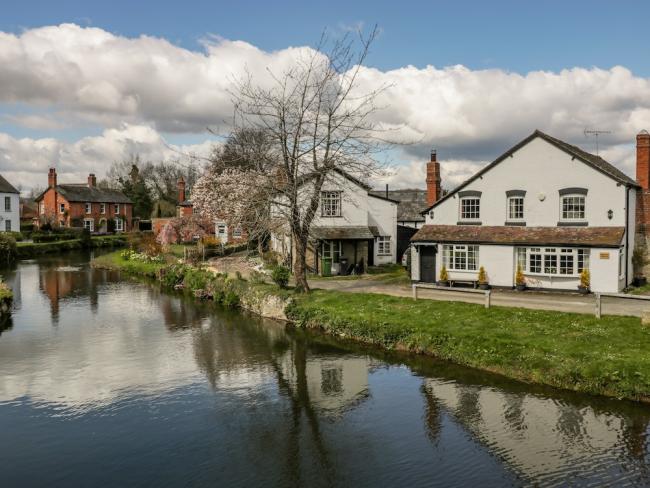 A Herefordshire riverside cottage with bay windows is fronted by a grassy bank down to a wide river.