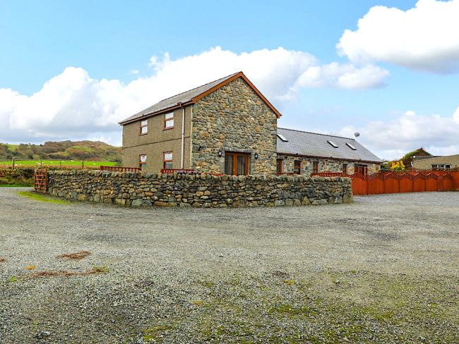 A Welsh stone-built barn conversion surrounded by a low stone wall in a large courtyard.