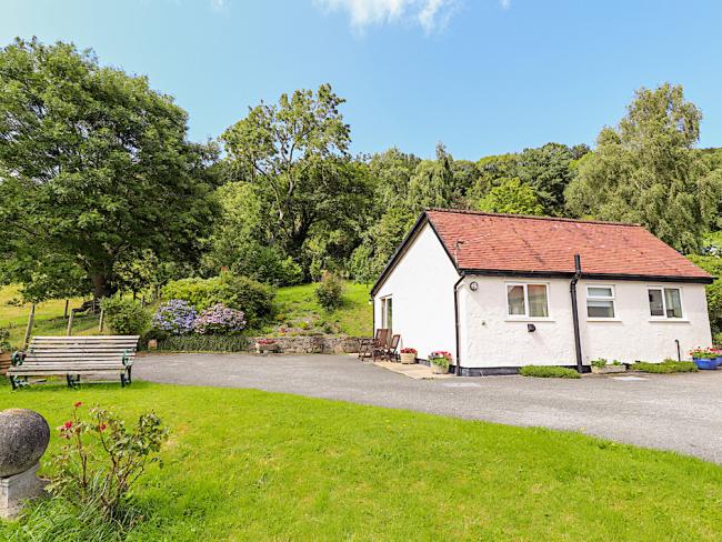 A countryside bungalow at the head of a drive with mature trees in th background