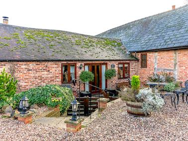 A single storey barn conversion  overlooks a courtyard full of shrubs in large pots.