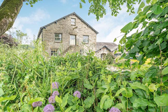 The 3-storey gable end seen through trees of a Cumbrian stone-barn conversion.