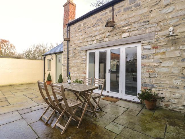 Singl storey barn convrsion with floor-to-ceiling windows and a flagstone terrace with dining table.