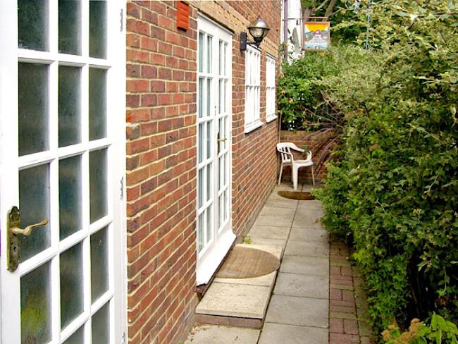 A paved path leads to the side entrance of a brick built, Isle-of-Wight holiday cottage 