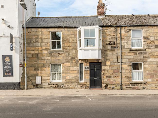 A stone-built terraced cottage with a large, 1st floor bay window overlooks a quiet street.
