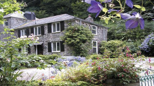 2-storey, granite-built cottage with many windows overlooks a mature garden.