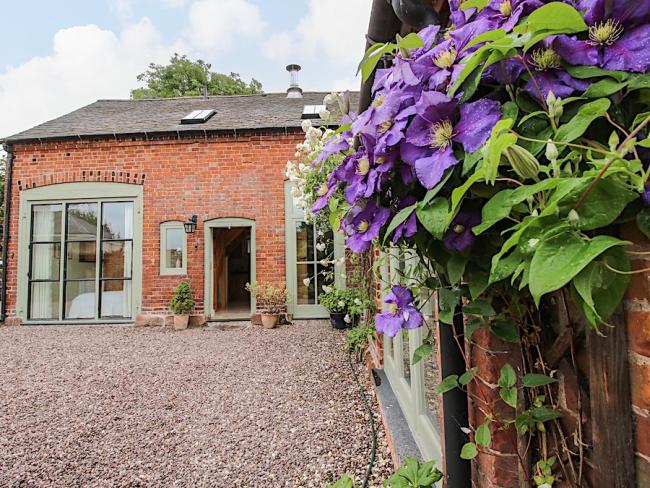 A flowering vine cimbs the walls of aconvrted coach house overlooking a courtyard in Shropshire