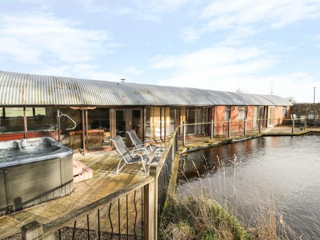 A row of wooden holiday lodges with a hot tub overlook a lake.