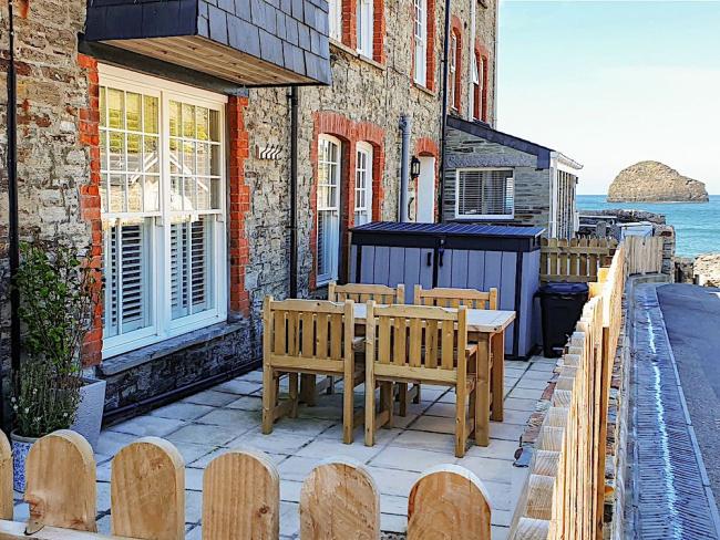 Stone built exterior of a Victorian, terraced holiday cottage with a fenced-in paved courtyard garden and sea views.