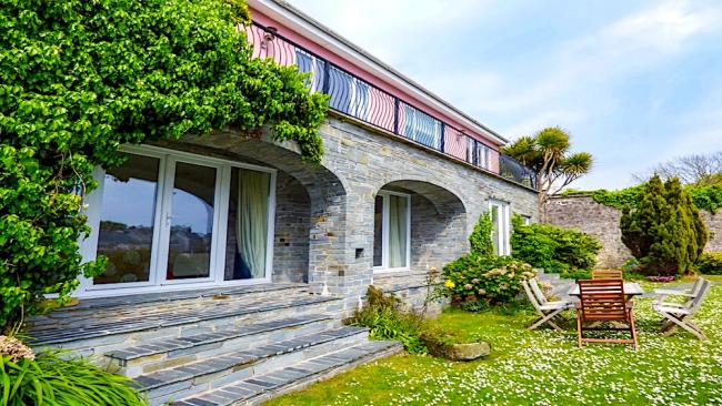 A wisteria-clad Tenby holiday cottage with floor-to-ceiling windows overlooks a daisy-filled lawn.