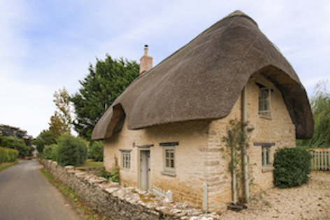 Exterior of a thatched 2-storey village holiday cottage in the Cotswolds.