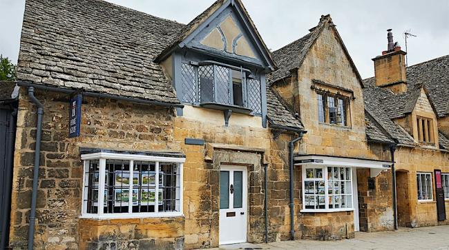 A semi-detached Cotswold holiday cottage with leaded, bay windows overlooks a village street.
