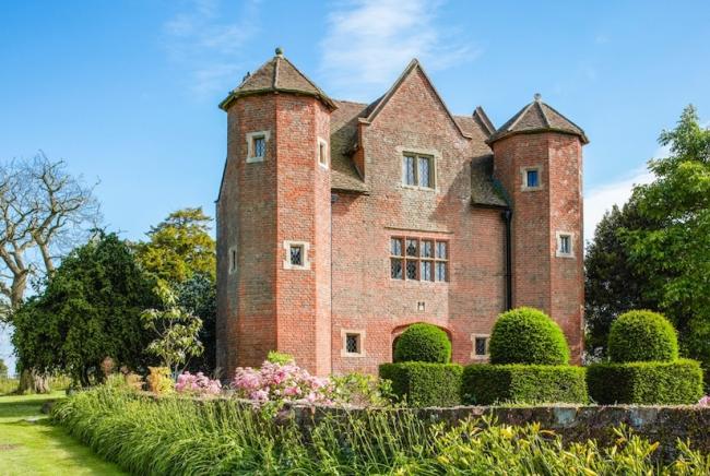 Exterior of a 3-storey, brick-built Tudor house with twin turrets and walled garden.