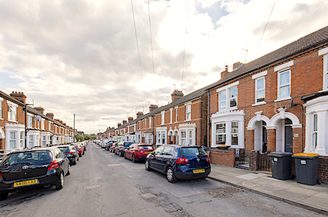 A terrace of brick-built Victorian houses with large bay windows overlook a street.