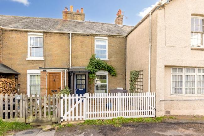 A stone-built terraced cottage with a front garden behind a picket fence.