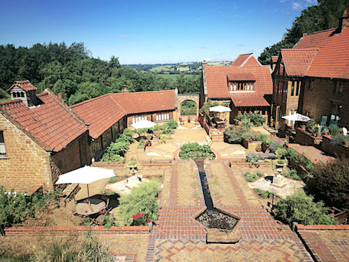 A flower-filled, paved formal garden courtyard surrounded by large and small barn conversions