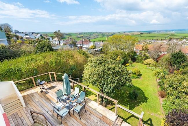 A 1st floor deck with outdoor dining furniture overlooks a garden and South Devon countryside.
