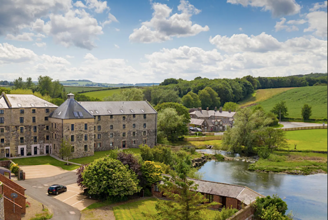 A converted 3-storey mill building overlooking lawns and a lake.