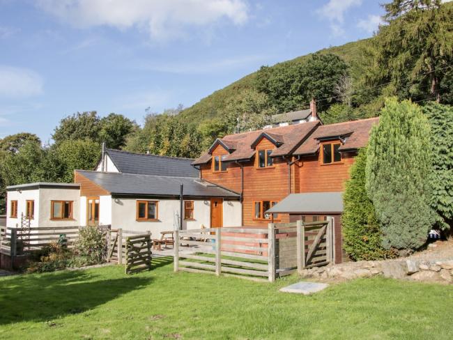 A wooden-clad Shropshire holiday home overlooks a lawn backed by trees.